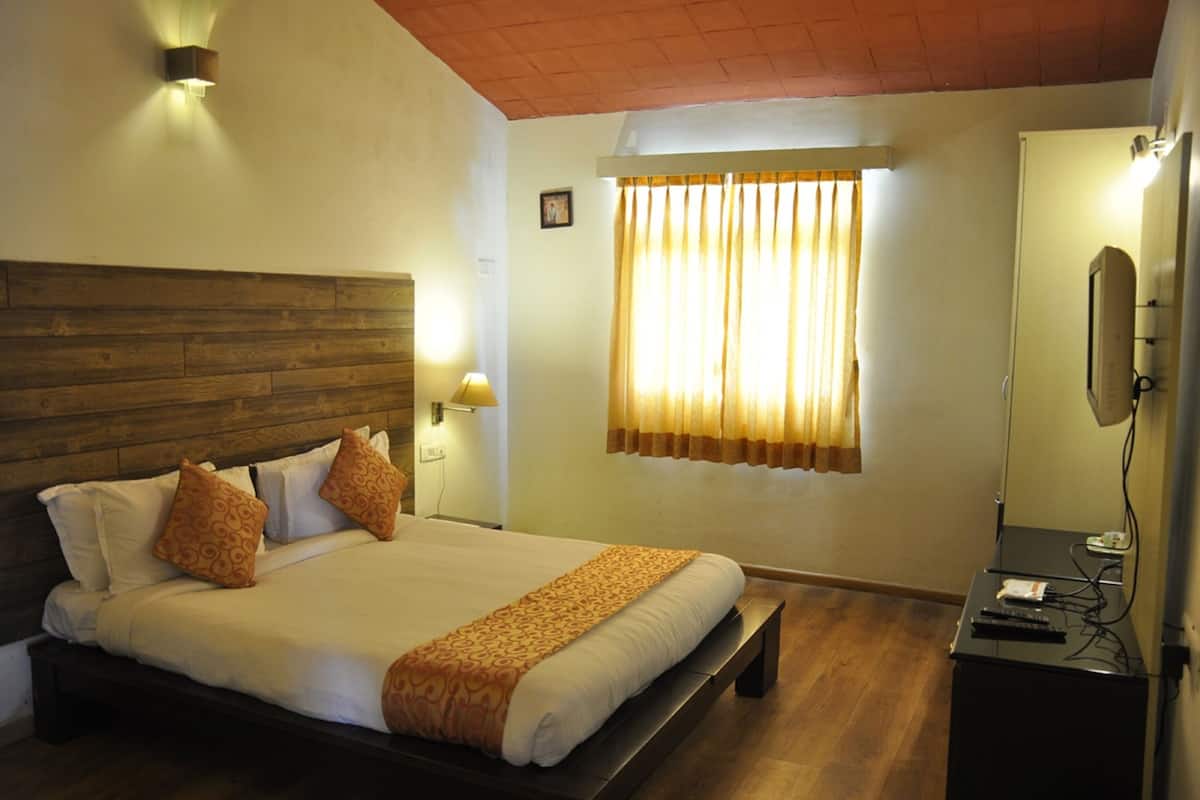 A hotel room with a wooden headboard, a large bed with white linens, a bedside table with a lamp, a window with curtains, and a television on a stand.