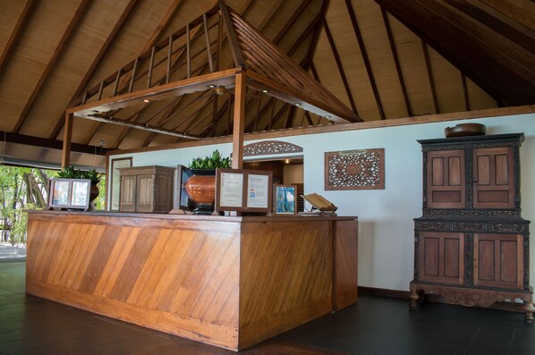 Un espace d’accueil comprenant un comptoir de réception en bois, un grand meuble décoratif et un plafond avec des poutres apparentes.