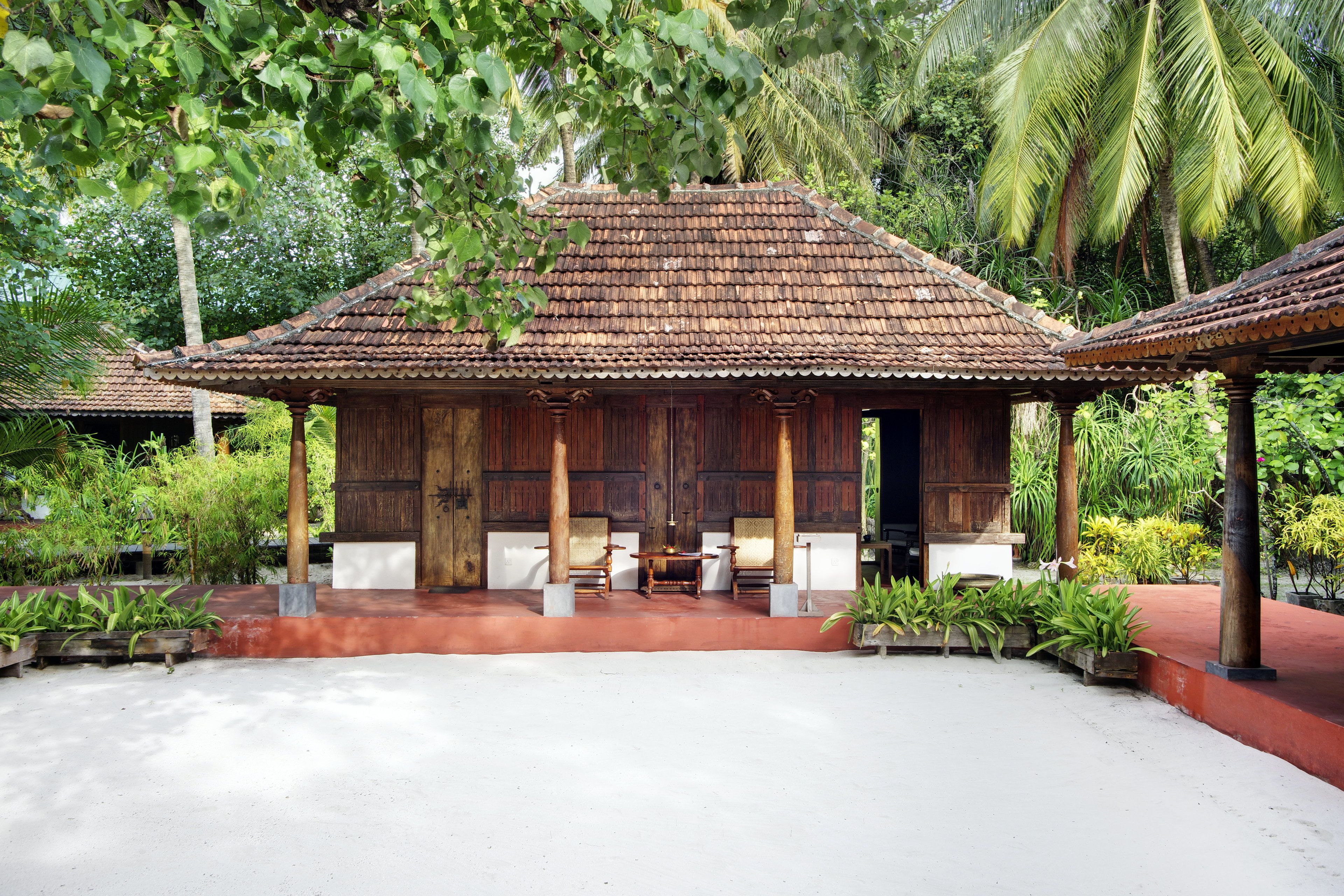 A traditional wooden building with a tiled roof, surrounded by lush greenery and palm trees.