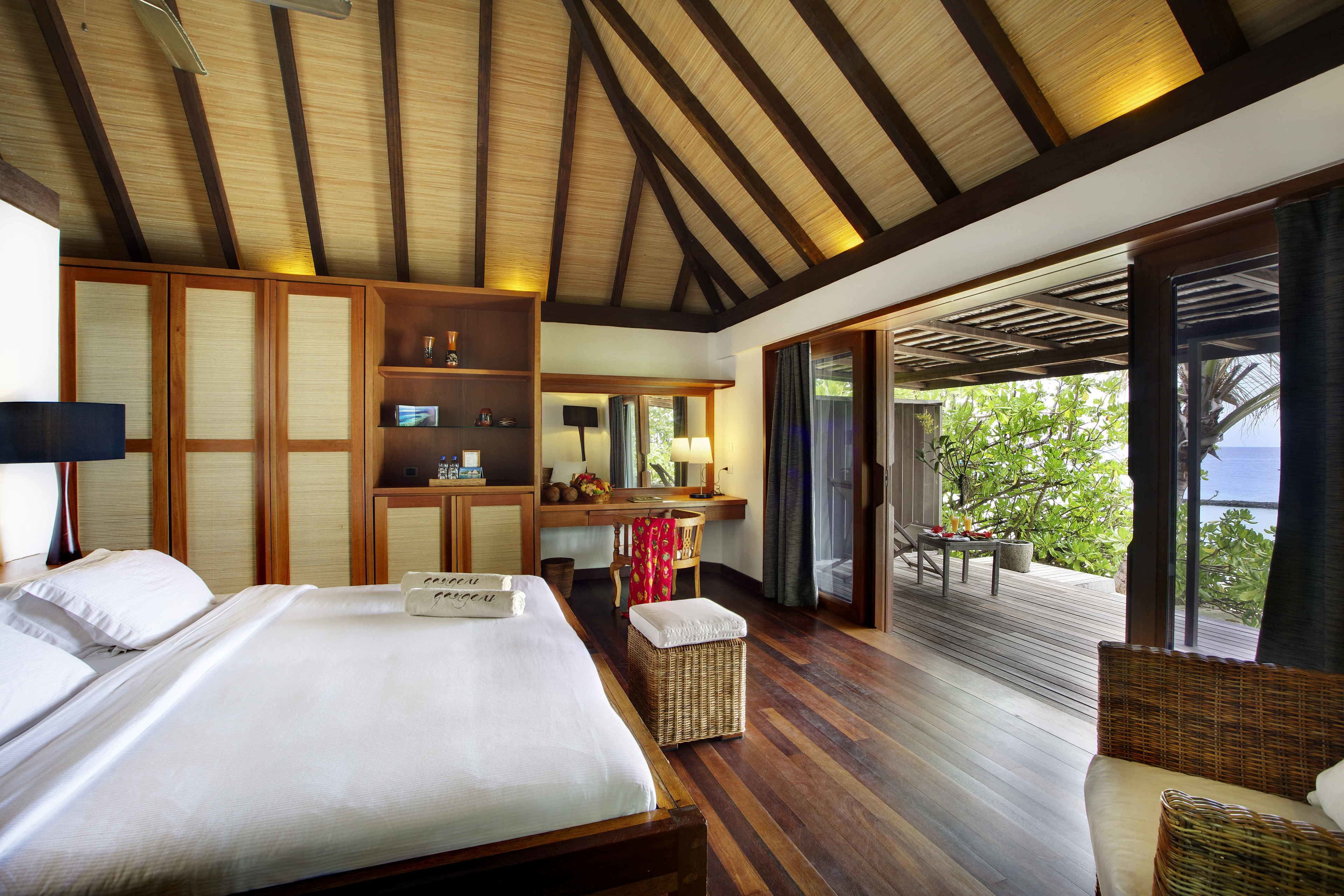A hotel room with a large bed, a desk, a chair, and a balcony with a view of greenery.