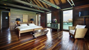 A spacious bedroom with a large bed, a wooden chest, and a wicker chair. - Gangehi Island Resort (Gangehi Island)