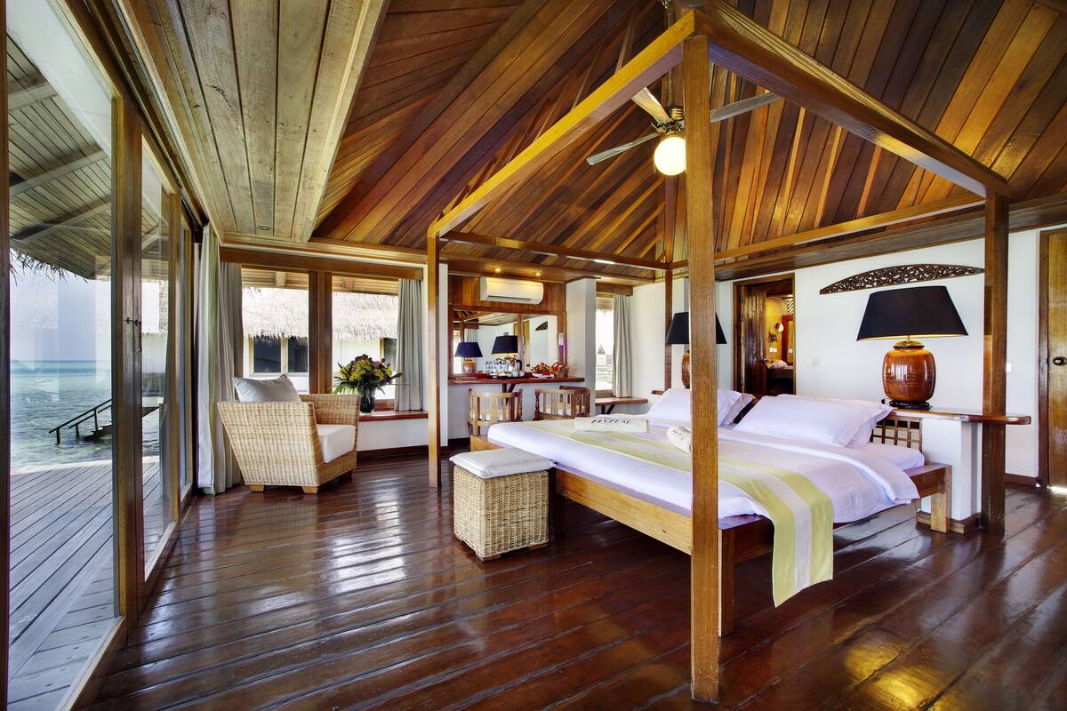 Una habitación amplia con techo de madera, una cama grande, una silla de mimbre y vista al océano.