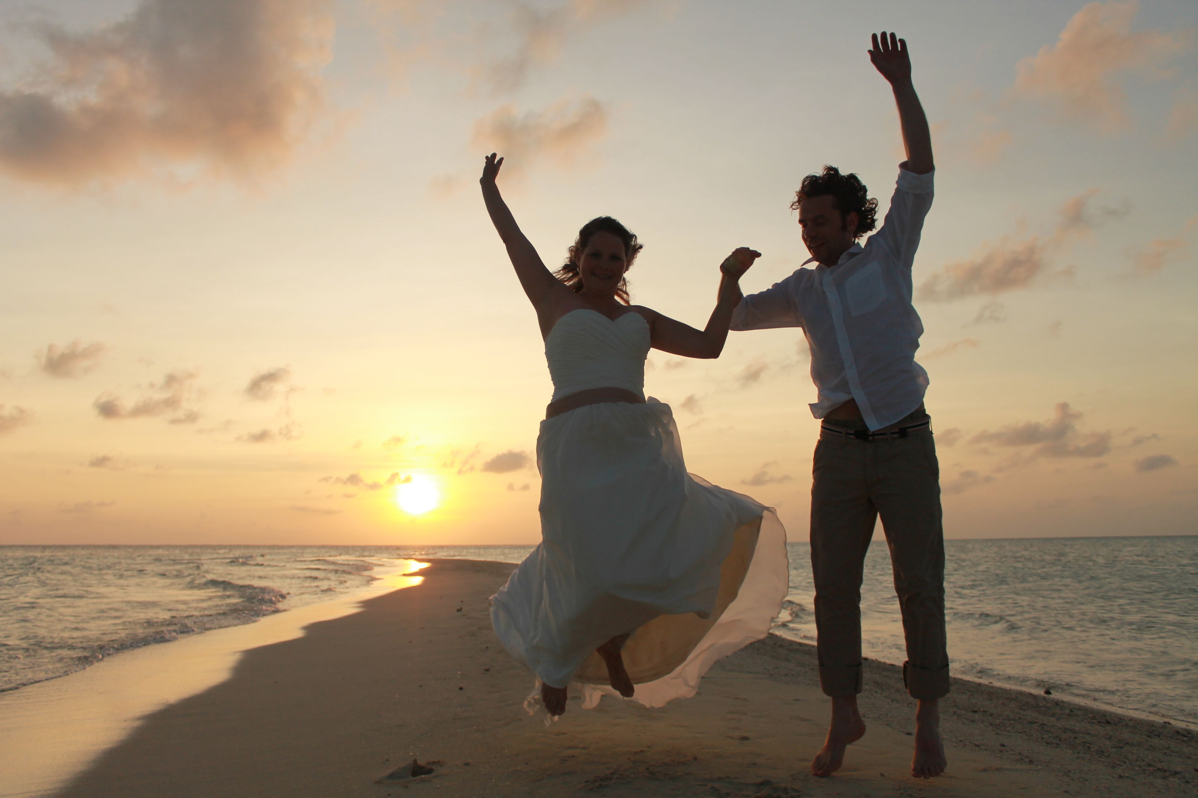 Um casal dançando na praia ao pôr do sol.