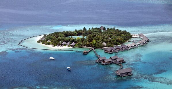 Een resort met bungalows boven het water, helder turquoise water, een klein zandstrand en een steiger.