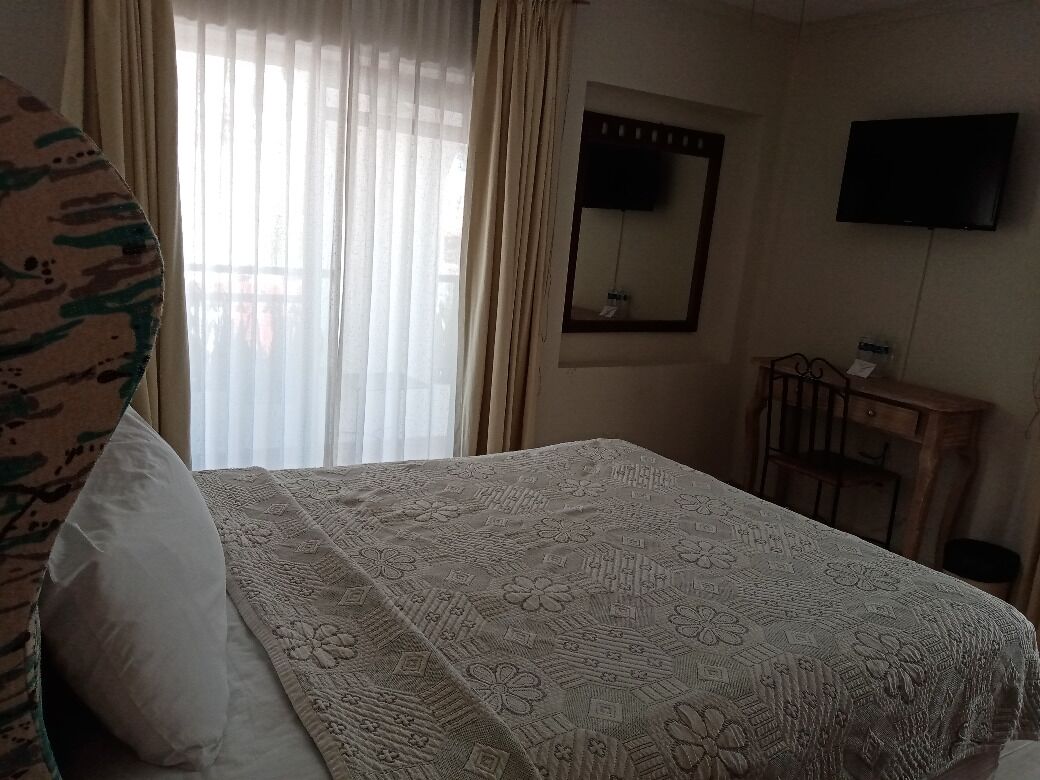 Una habitación de hotel con cama, escritorio, silla, televisión y ventana con cortinas.