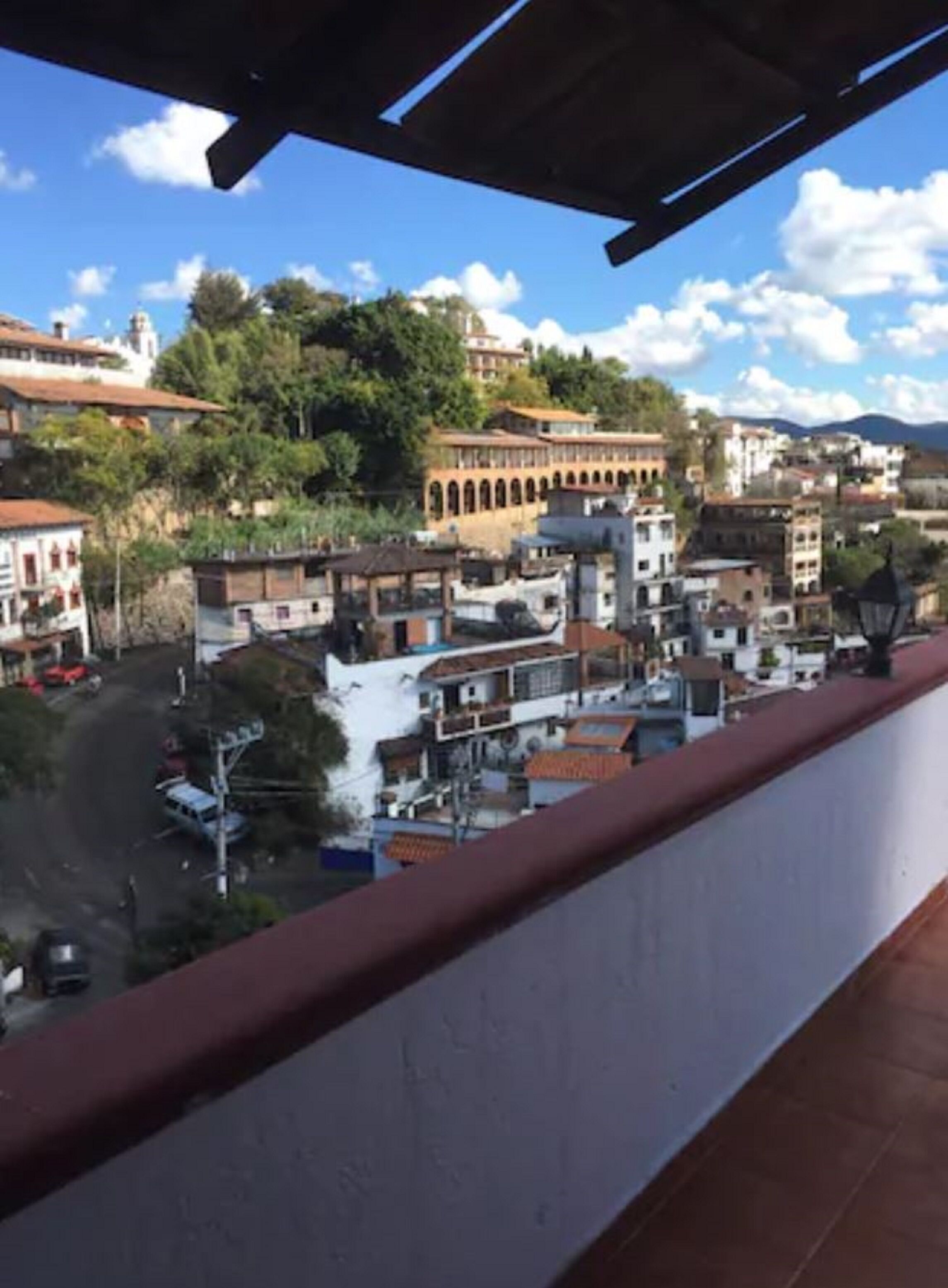 A balcony overlooking a town with buildings, a road, and greenery.
