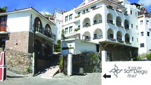 A multi-story hotel with a white facade, arched balconies, and a stone base. - Hotel Real de San Diego (Taxco)