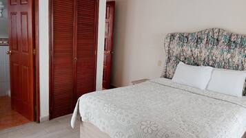 A bedroom with a bed, a nightstand, a wooden wardrobe, and a patterned headboard.