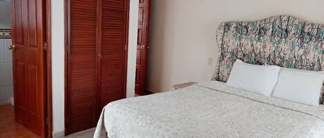 Un dormitorio con una cama, una mesita de noche, un armario de madera y un cabecero estampado.