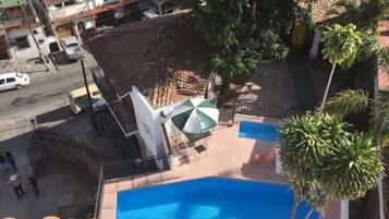 A residential area with a swimming pool, a white building with a green umbrella, and a street with parked cars.
