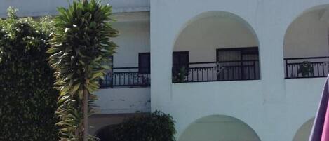 A multi-story building with balconies, a swimming pool, and lush greenery.