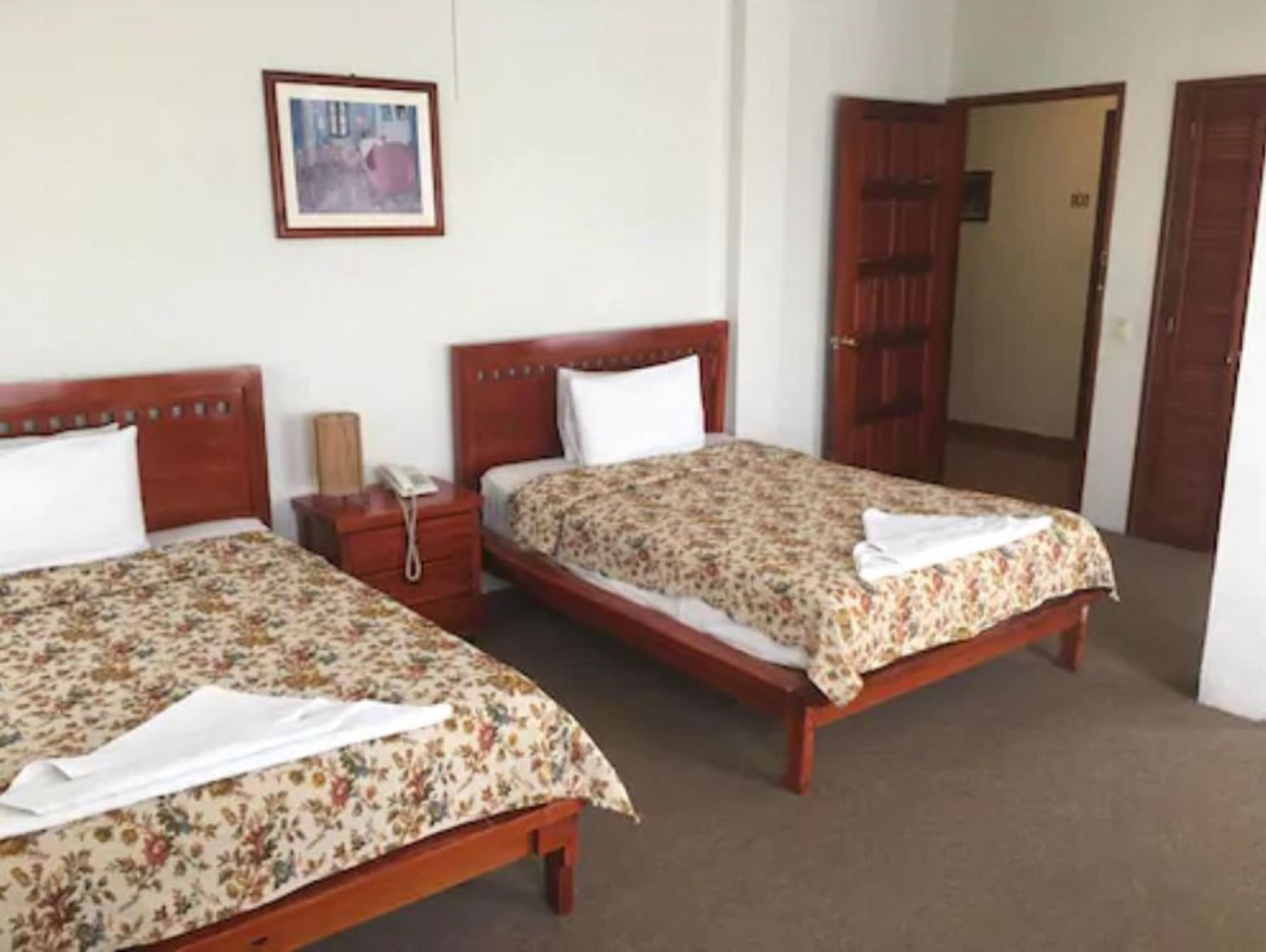 Due letti matrimoniali con coperte a fiori, testiere in legno, un comodino con una lampada e un quadro appeso al muro.