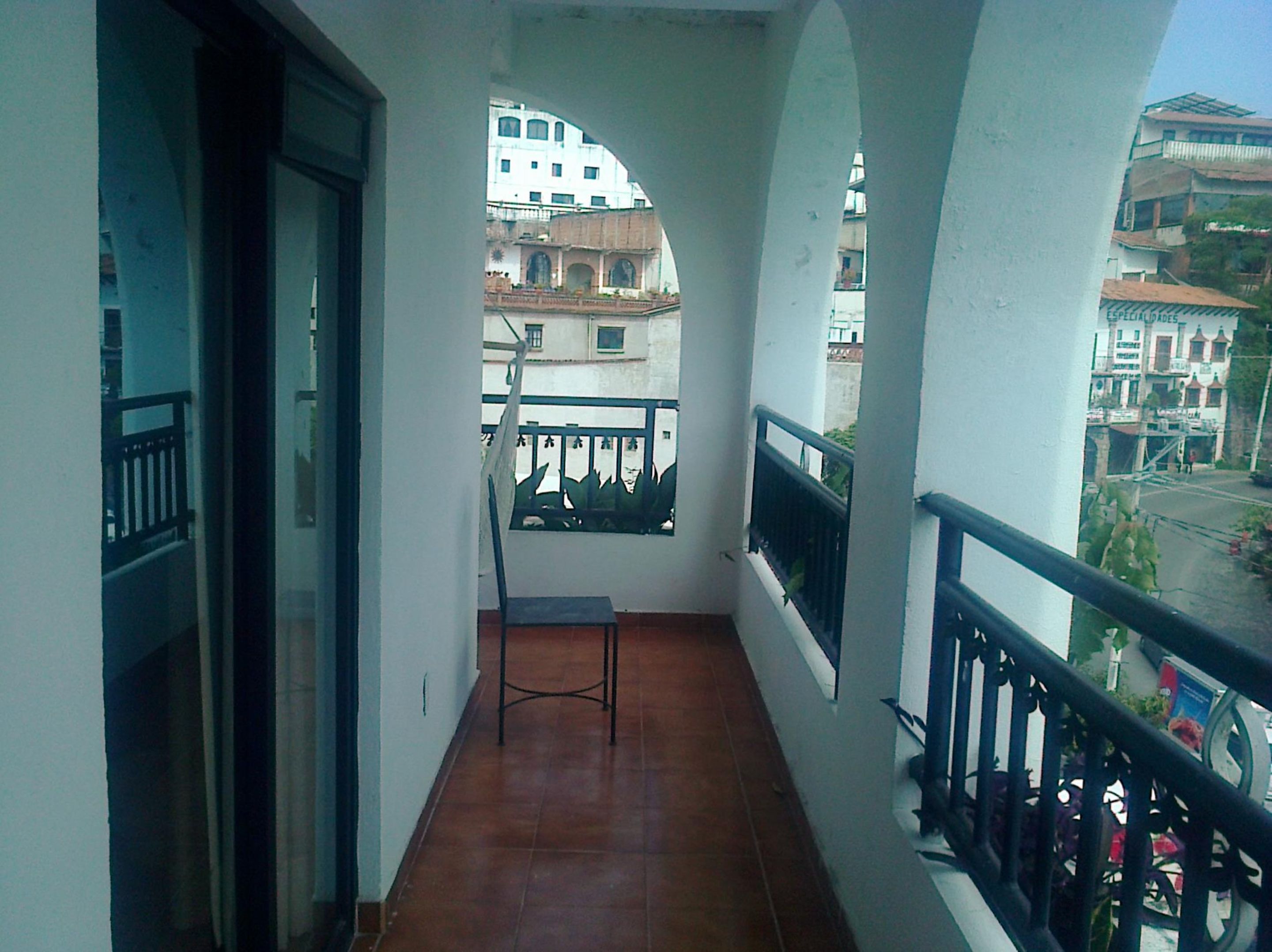 A balcony with a chair, a view of buildings, and a tiled floor.