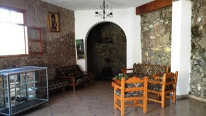 A living room with a stone wall, a glass display cabinet, a wooden dining table with chairs, and a sofa. - Hotel Real de San Diego (Taxco)