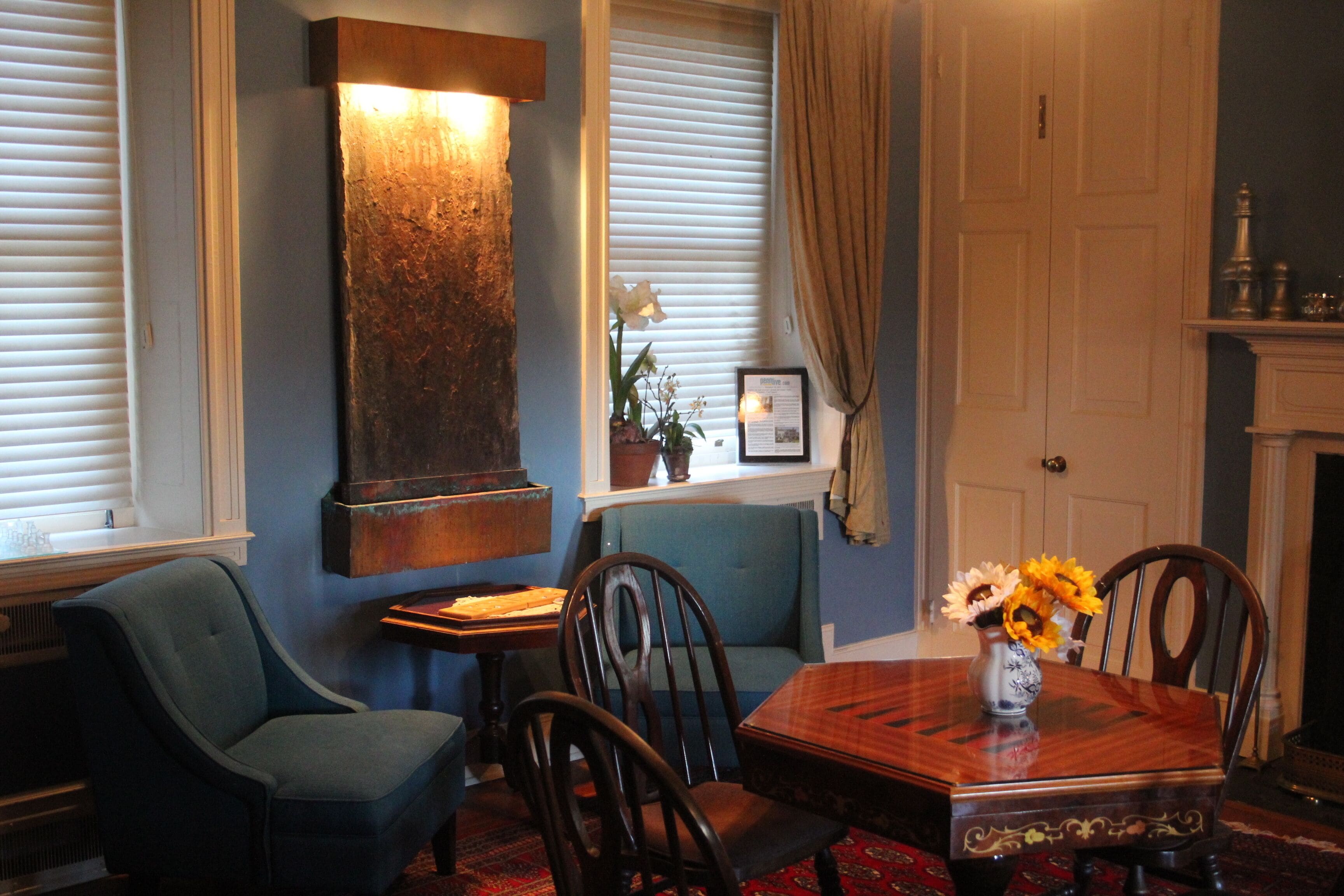 A dining area with a wooden table, chairs, a vase with flowers, a blue sofa, and a fireplace.