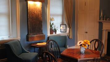 A dining area with a wooden table, chairs, a vase with flowers, a blue sofa, and a fireplace.