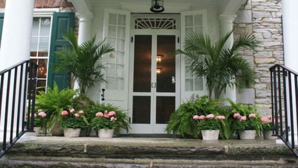 A white door with glass panels, flanked by two potted plants with pink flowers, leading to a stone staircase. - Stocks Manor Bed and Breakfast (Mechanicsburg)