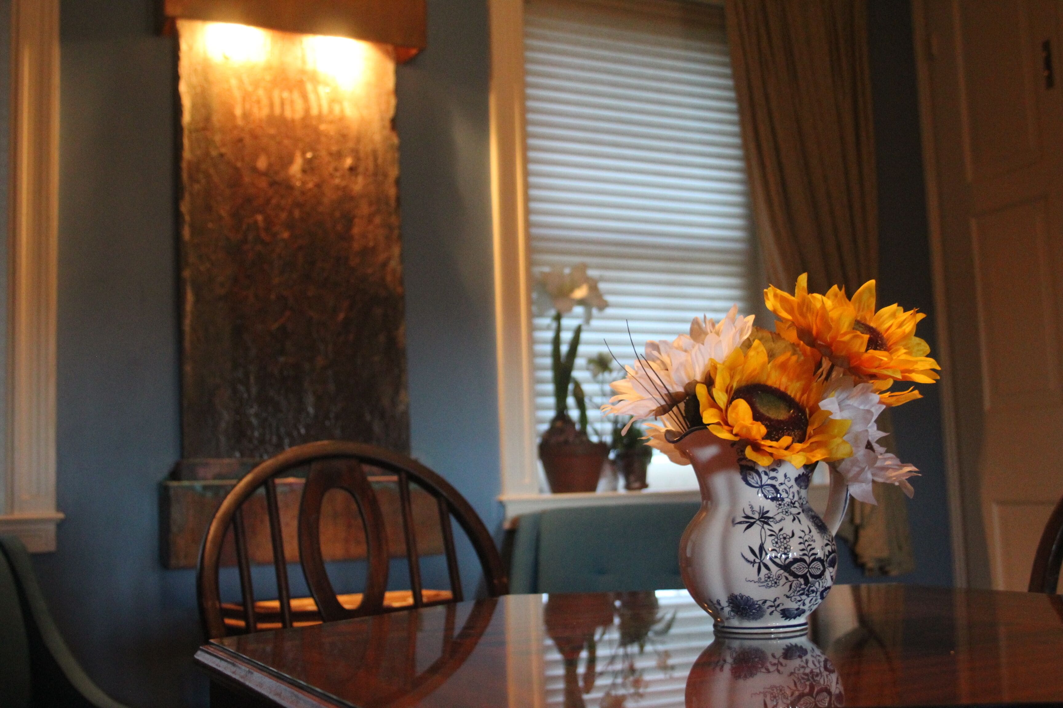 Una mesa de comedor con un florero, una silla de madera y una lámpara fijada a la pared.