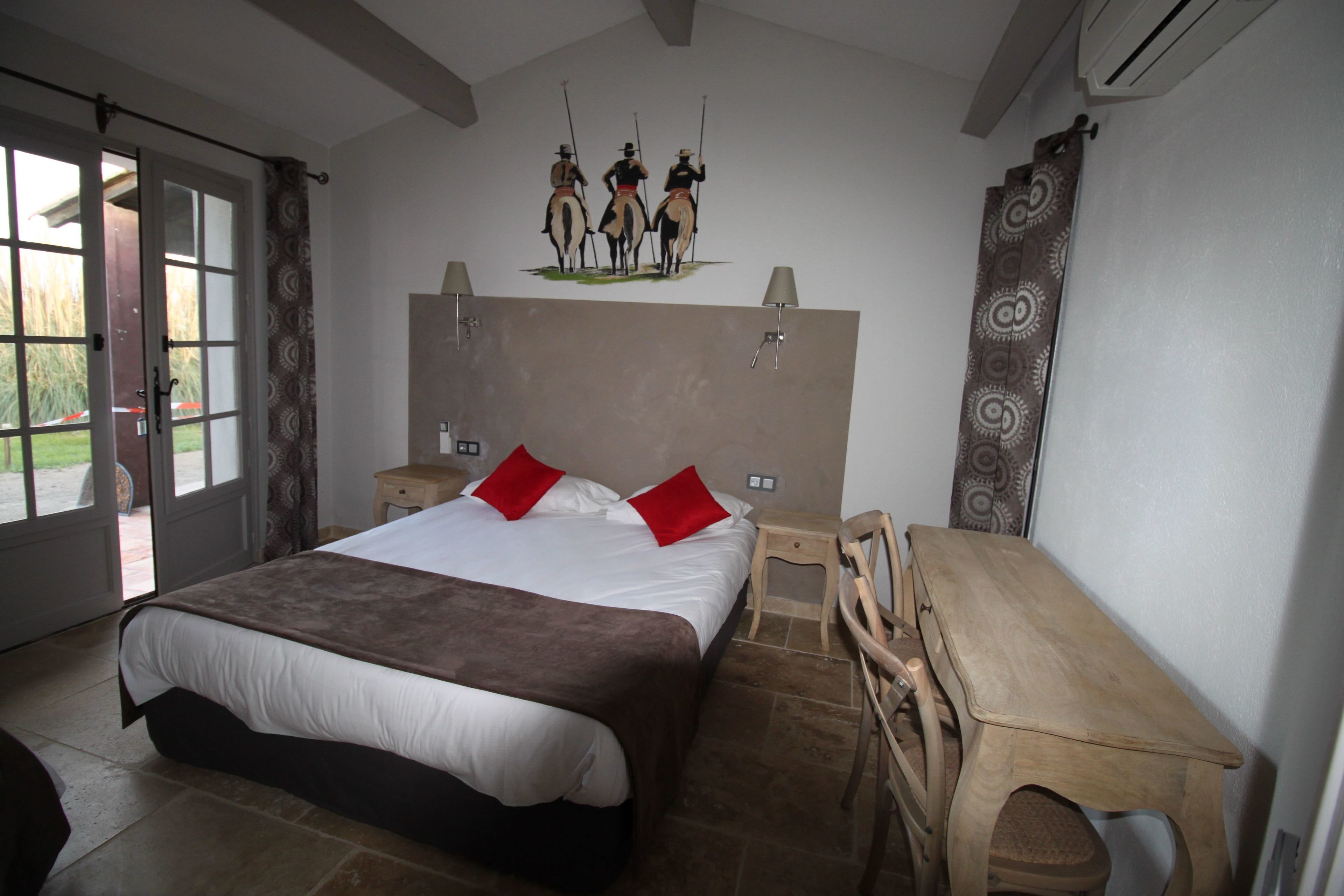 Een slaapkamer met een groot bed, een houten bureau, een stoel, een nachtkastje en een wandlamp.