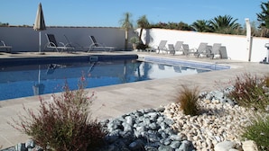 Una piscina con sillones de descanso y una sombrilla pequeña, rodeada de rocas y plantas.