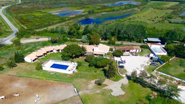 Vista aérea de una propiedad con piscina, varias construcciones y un área cercada con animales pastando.
