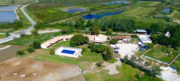 Vista aérea de una propiedad con piscina, varias construcciones y un área cercada con animales pastando.