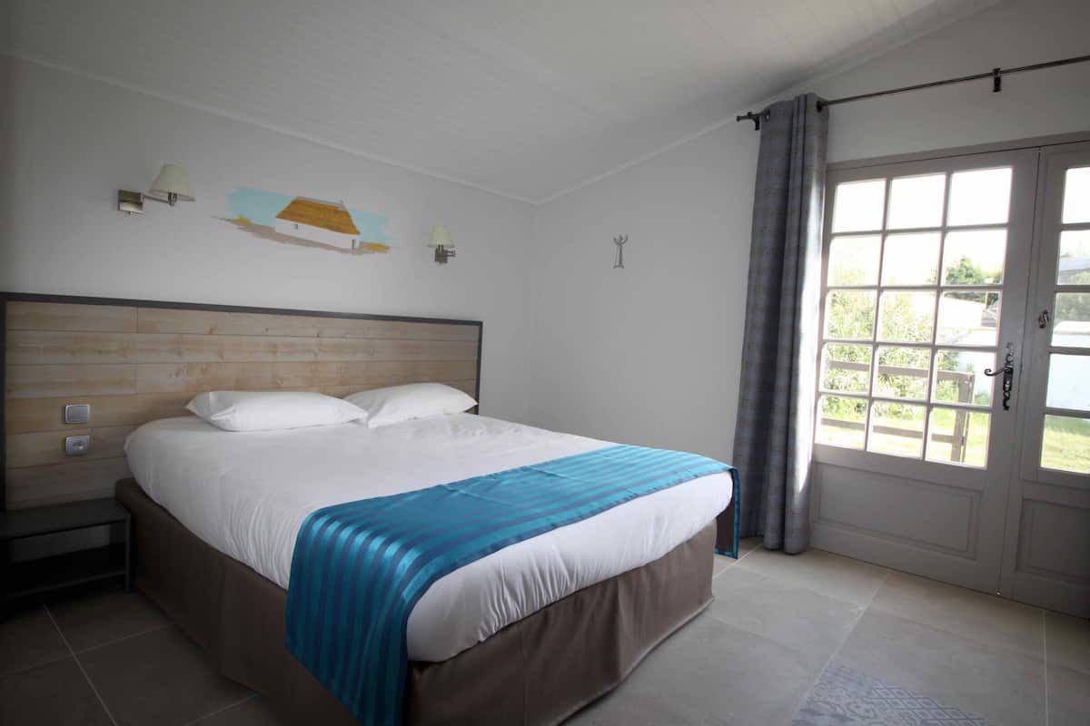 Ein Schlafzimmer mit einem großen Bett, einem Nachttisch, einem Fenster mit Vorhängen und einer Tür.