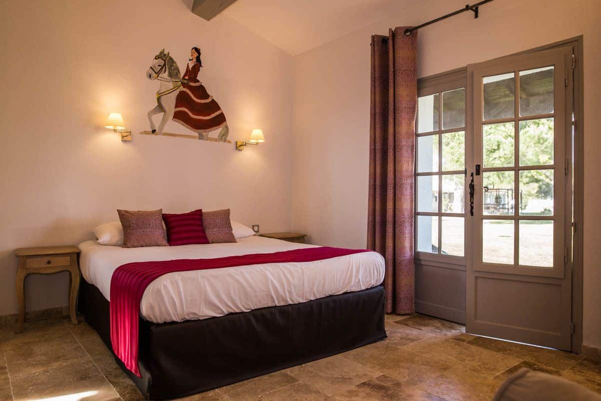 Ein Schlafzimmer mit einem großen Bett, einem Nachttisch, einer Wandlampe, einer Tür mit Blick und einem Vorhangfenster.