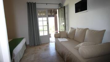Una habitación con cama, sofá, televisor y ventana con cortinas.