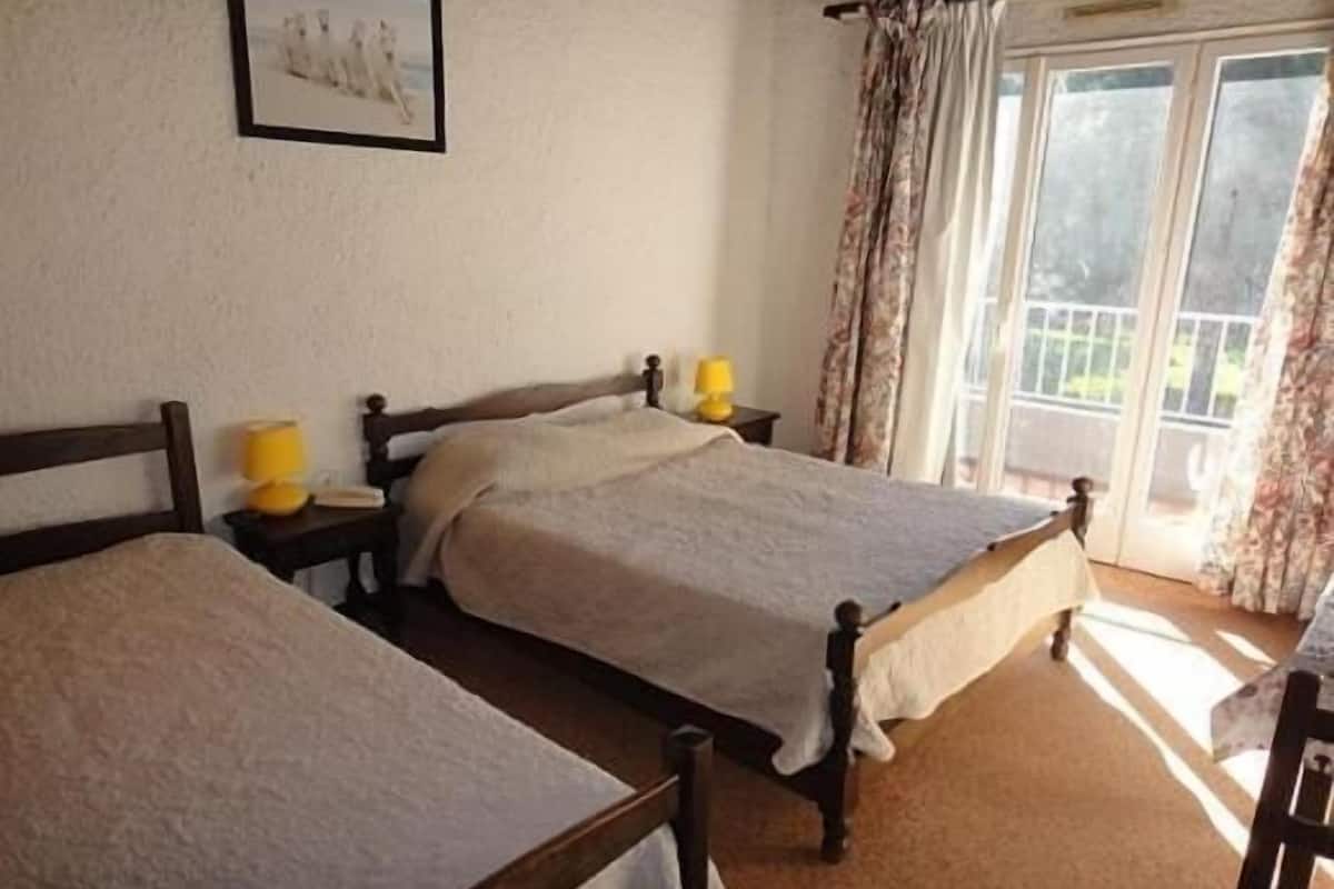 A bedroom with two wooden beds, a nightstand with a lamp, and a window with curtains.
