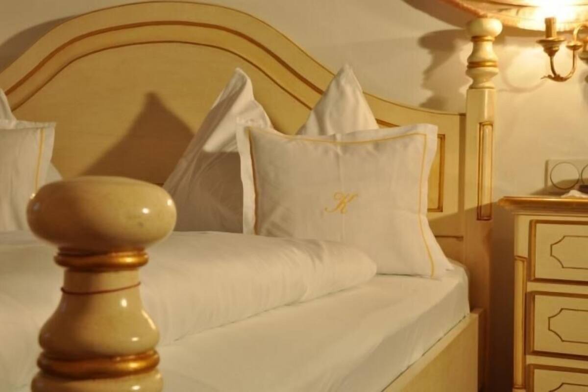 Un lit avec du linge de lit blanc et des touches dorées, une tête de lit en bois et une table de chevet avec des tiroirs.