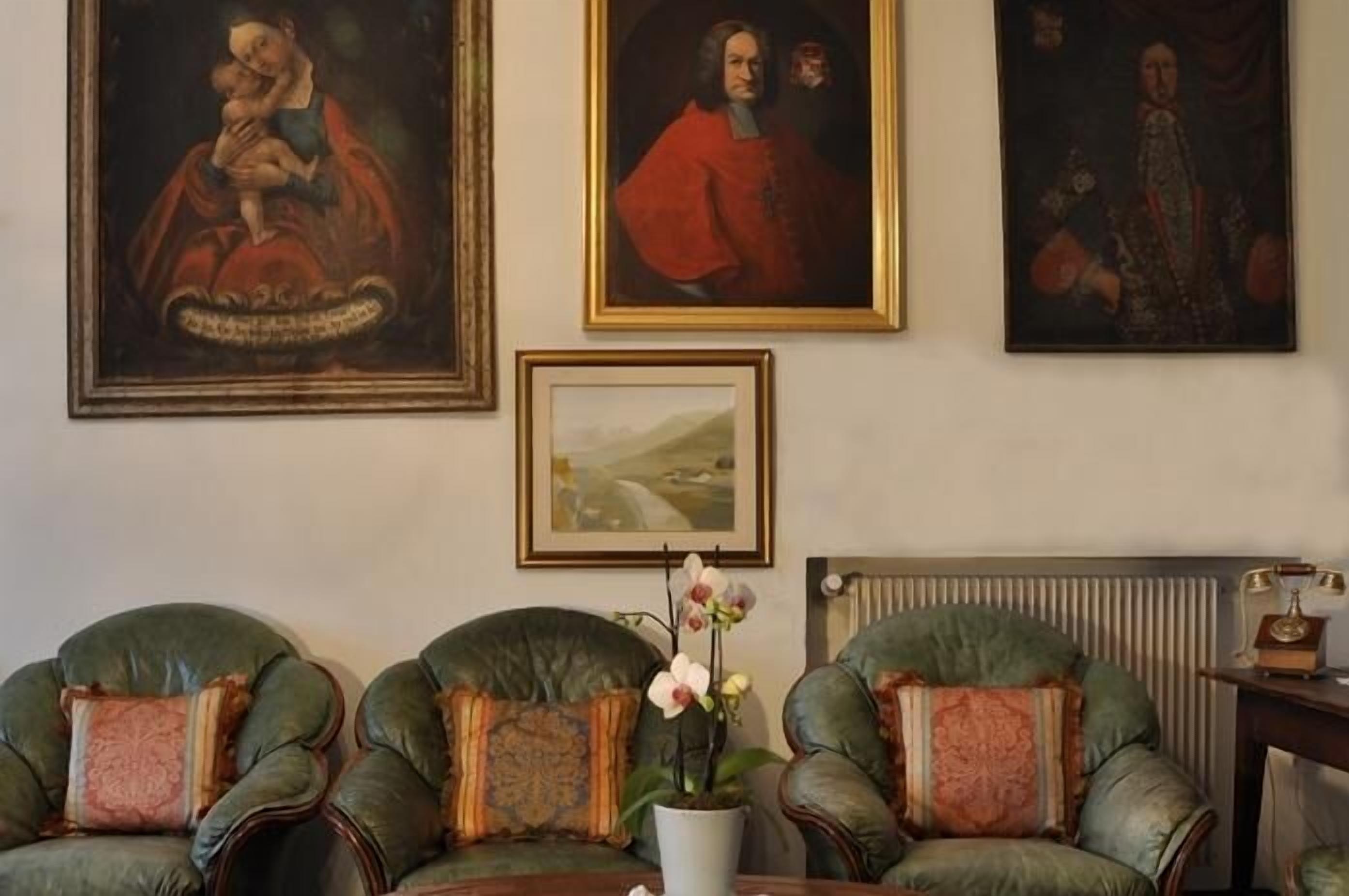 A room with three leather armchairs, a radiator, and three framed artworks on the wall.