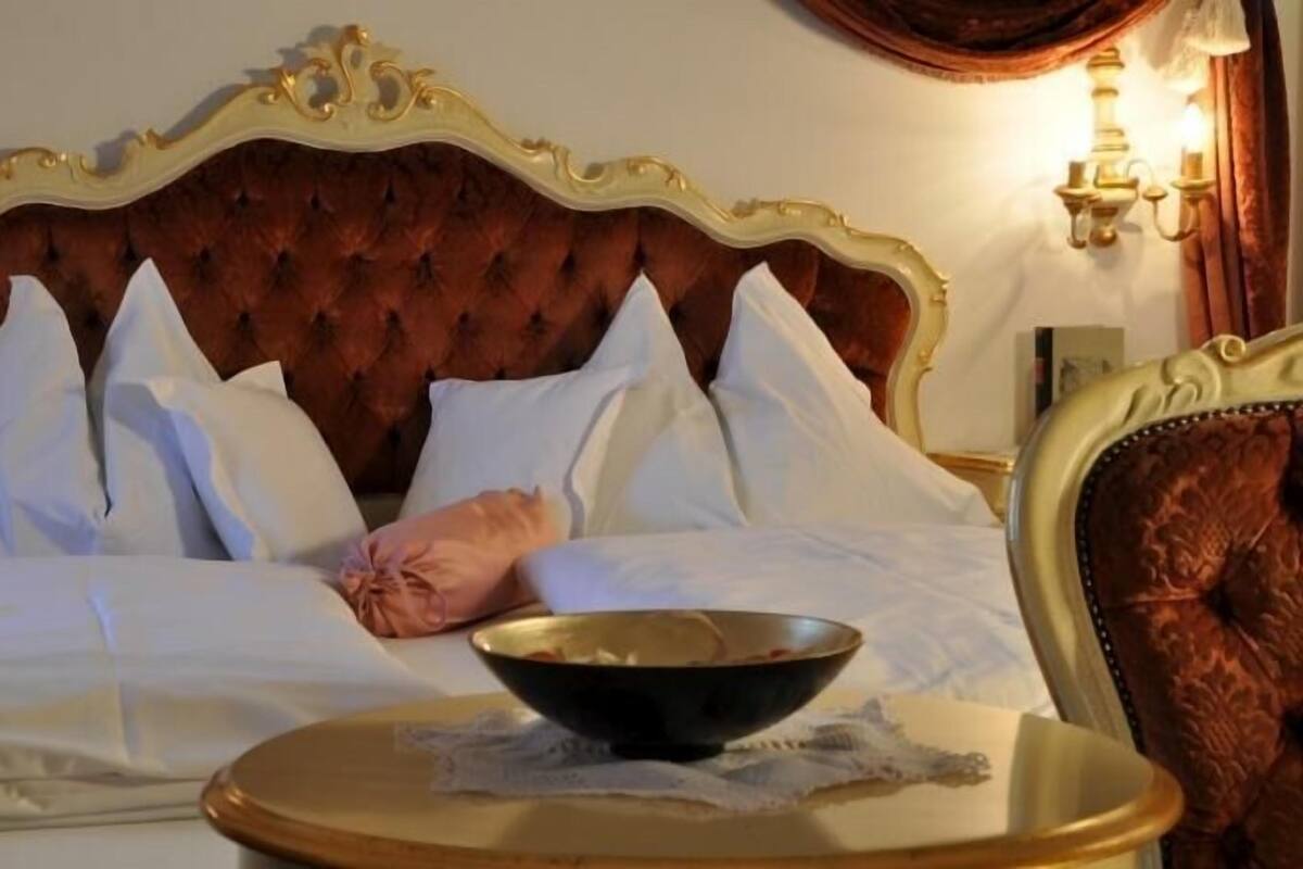 Une chambre d’hôtel avec une tête de lit capitonnée, du linge de lit blanc, un bol posé sur une table d’appoint et un luminaire fixé au mur.