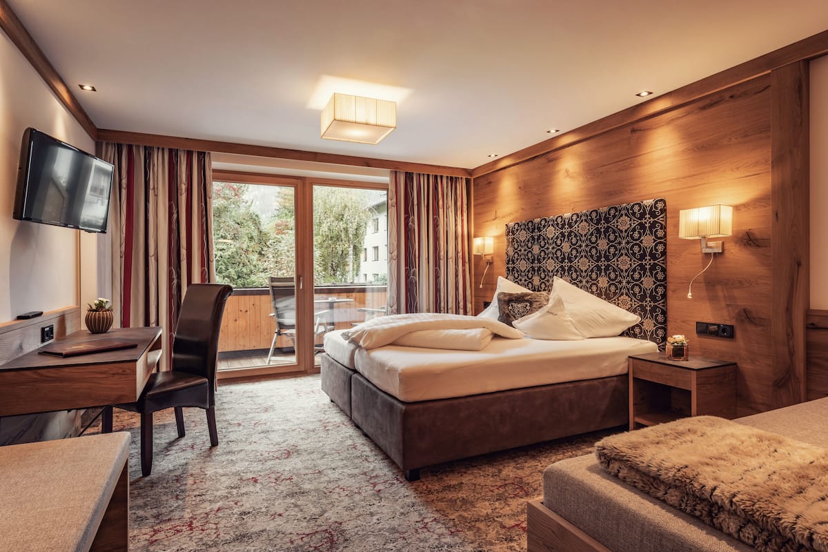 A hotel room with a bed, a desk, a chair, a TV, a window with curtains, and a balcony.