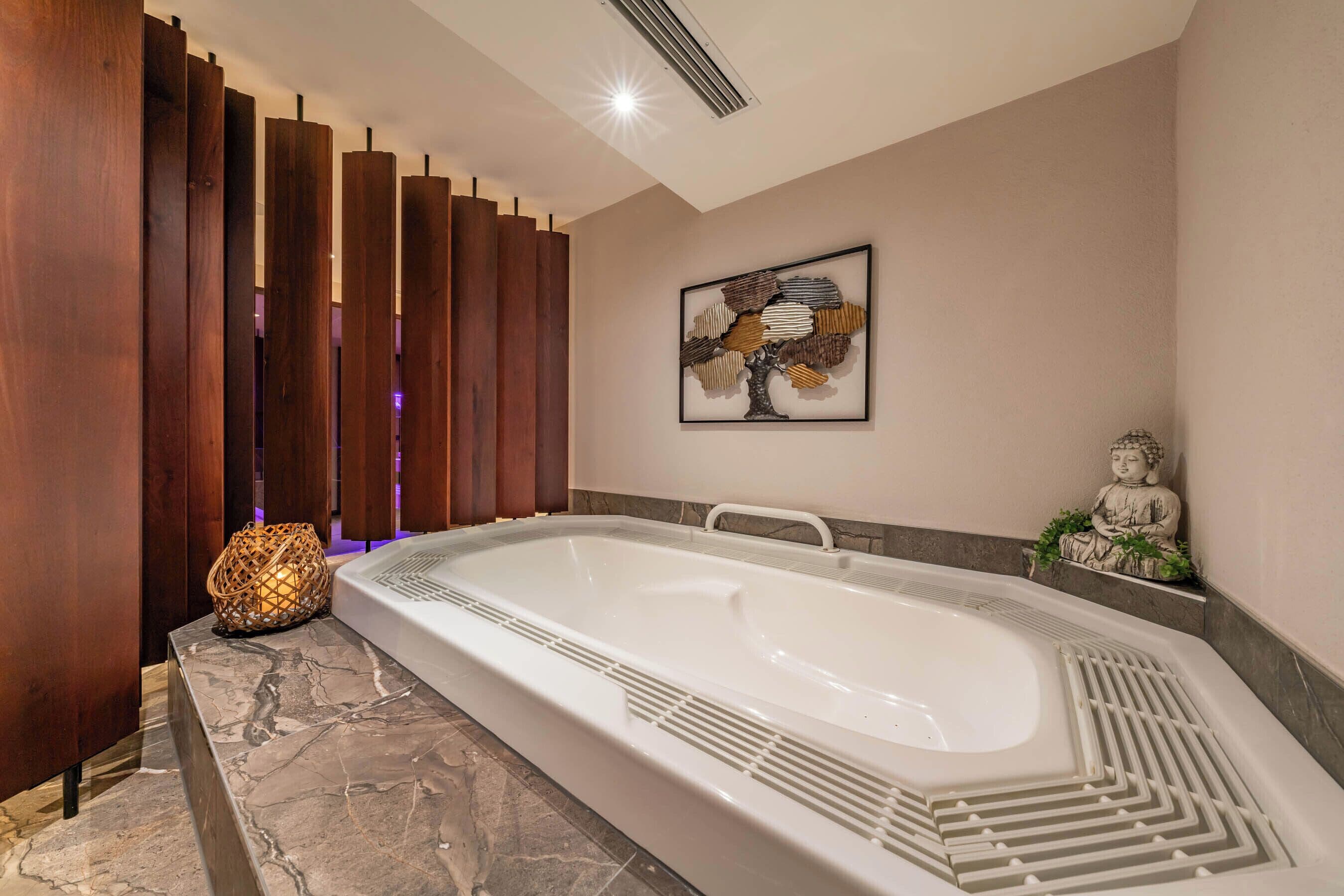 A modern bathroom with a large bathtub, wooden paneling, a decorative wall piece, and a statue.