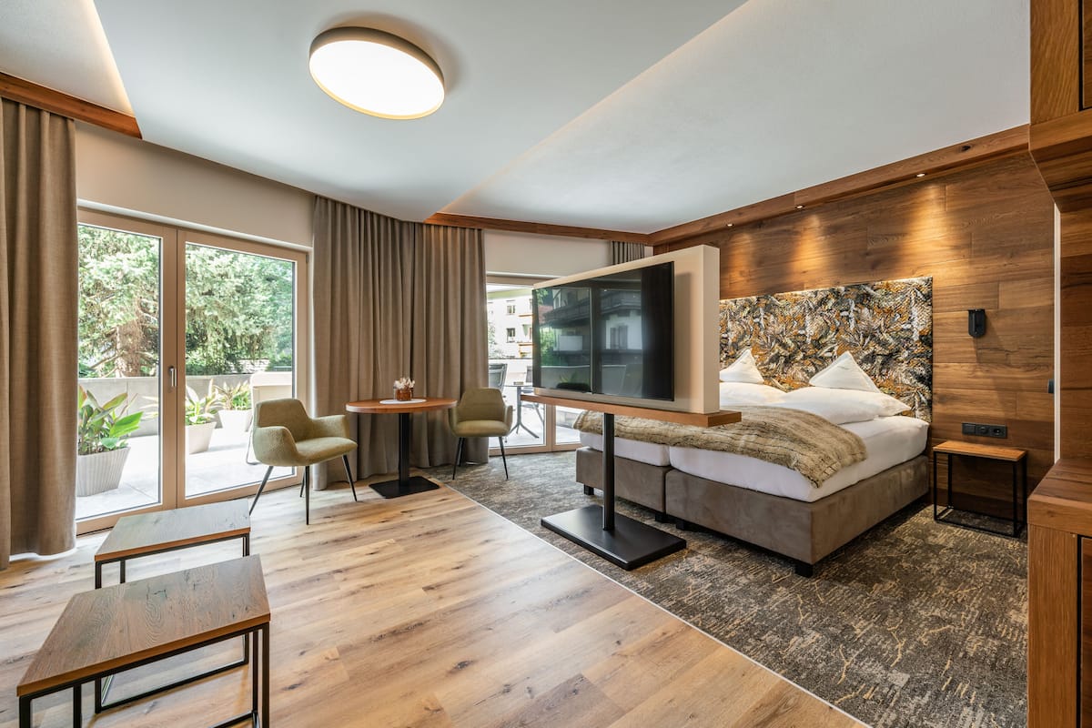 A modern hotel room with a large bed, a flat-screen TV, a dining area, and a view of the outdoors.