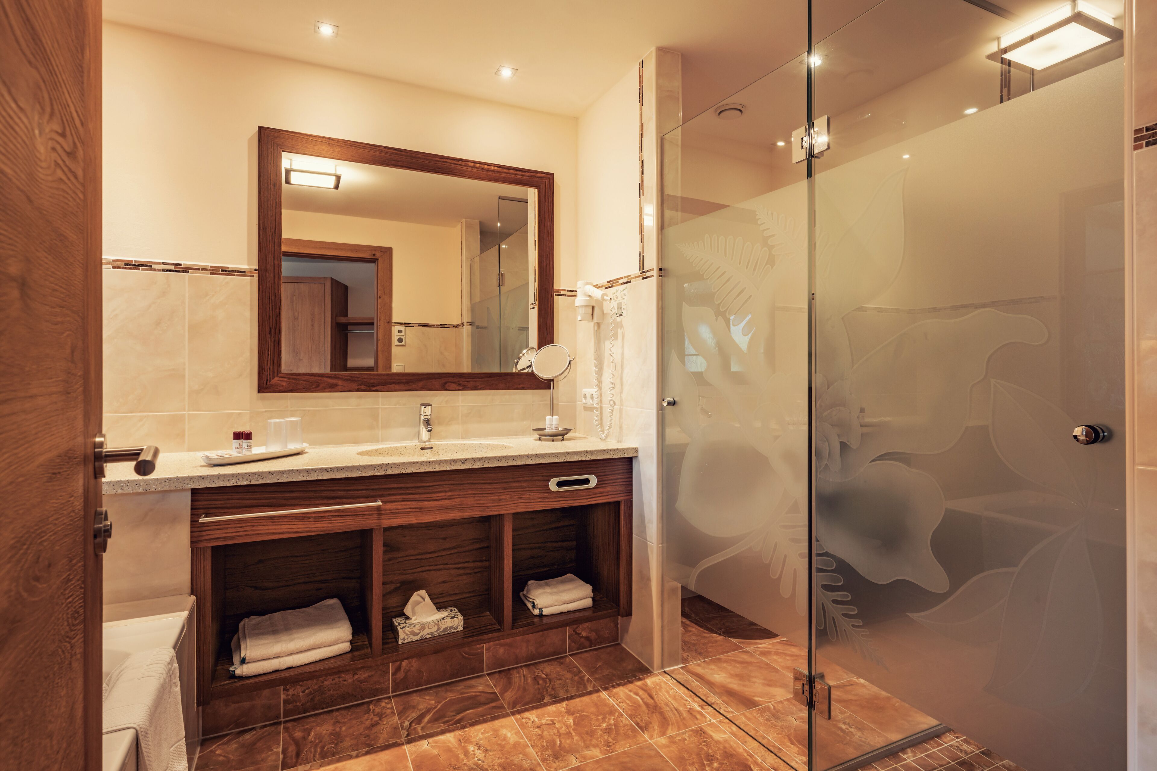 Un baño moderno con ducha de vidrio, tocador de madera con espejo y piso de mármol.