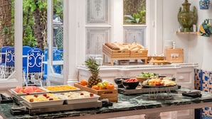 A breakfast buffet with various fruits and pastries, a tropical fruit centerpiece, and a view of the garden through large windows.