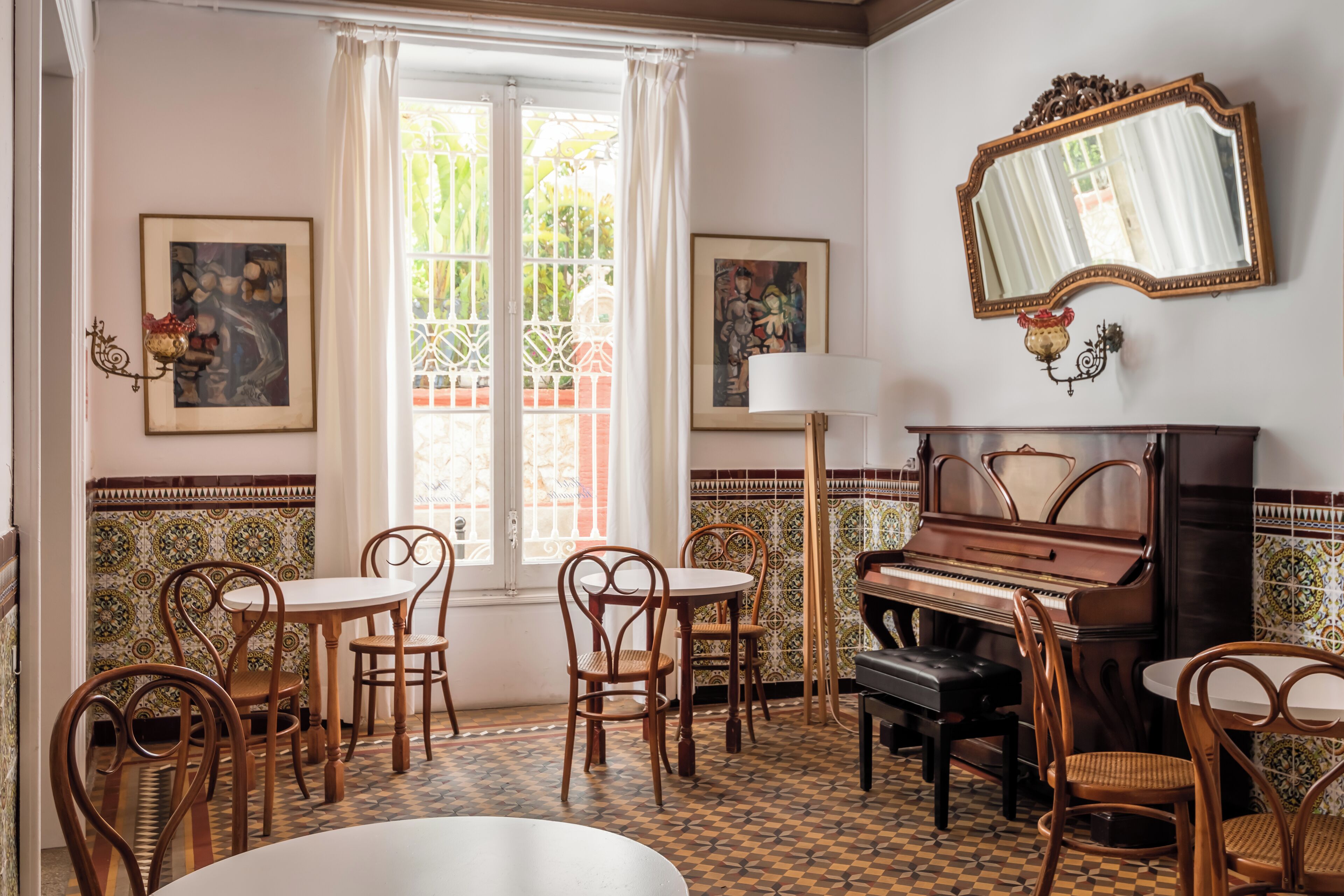 A dining area with a piano, chairs, a table, and a window with curtains.