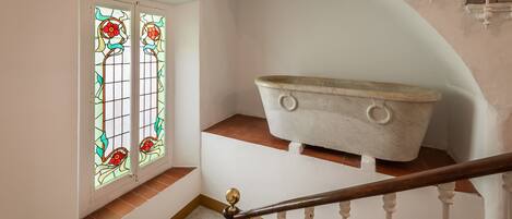 A bathroom with a bathtub, a stained glass window, and a staircase with a wooden handrail.