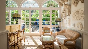 A sunlit room with wicker furniture, large arched windows, and decorative wall art.