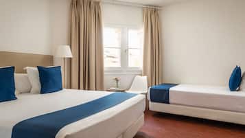 Ein Hotelzimmer mit zwei Betten, einem Fenster mit Vorhängen, einer Nachttischlampe und einem kleinen Tisch mit Blumen.