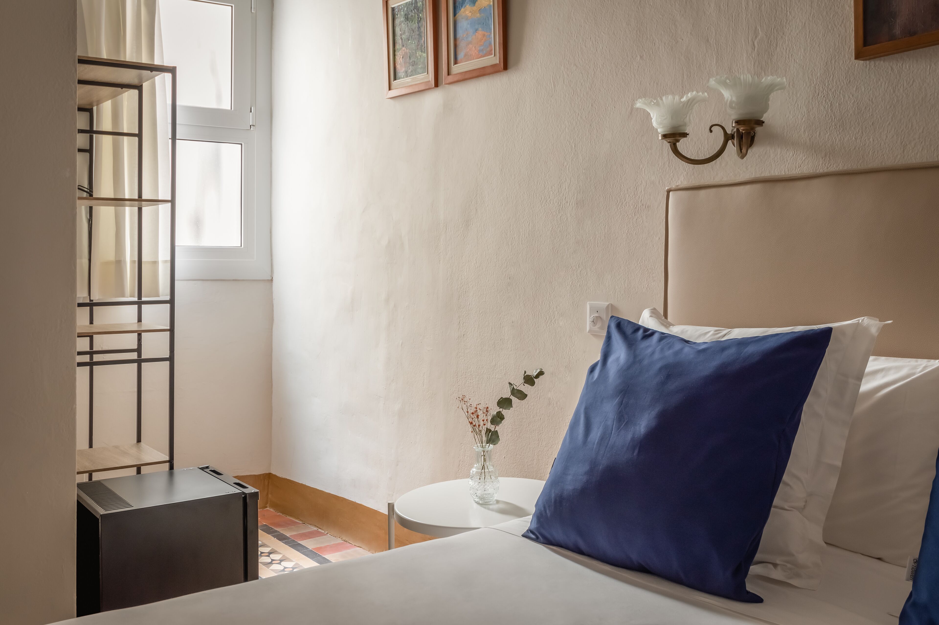 A bedroom with a bed, a small round table with a vase, and a window with curtains.