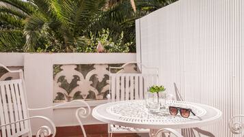 A round white metal table with two chairs, a small potted plant, and a pair of sunglasses on it.