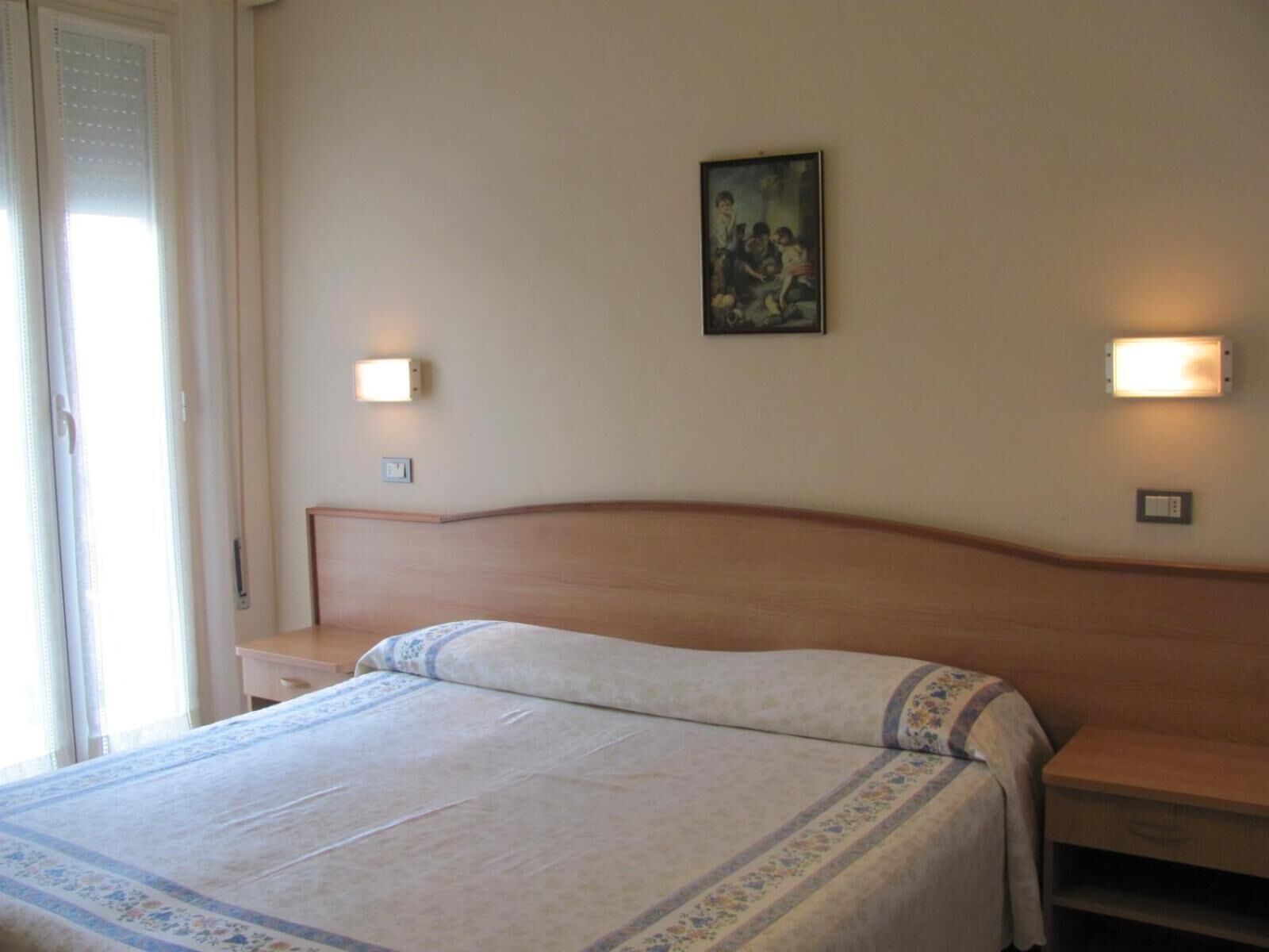 A hotel room with a bed, bedside tables, and wall-mounted lights.