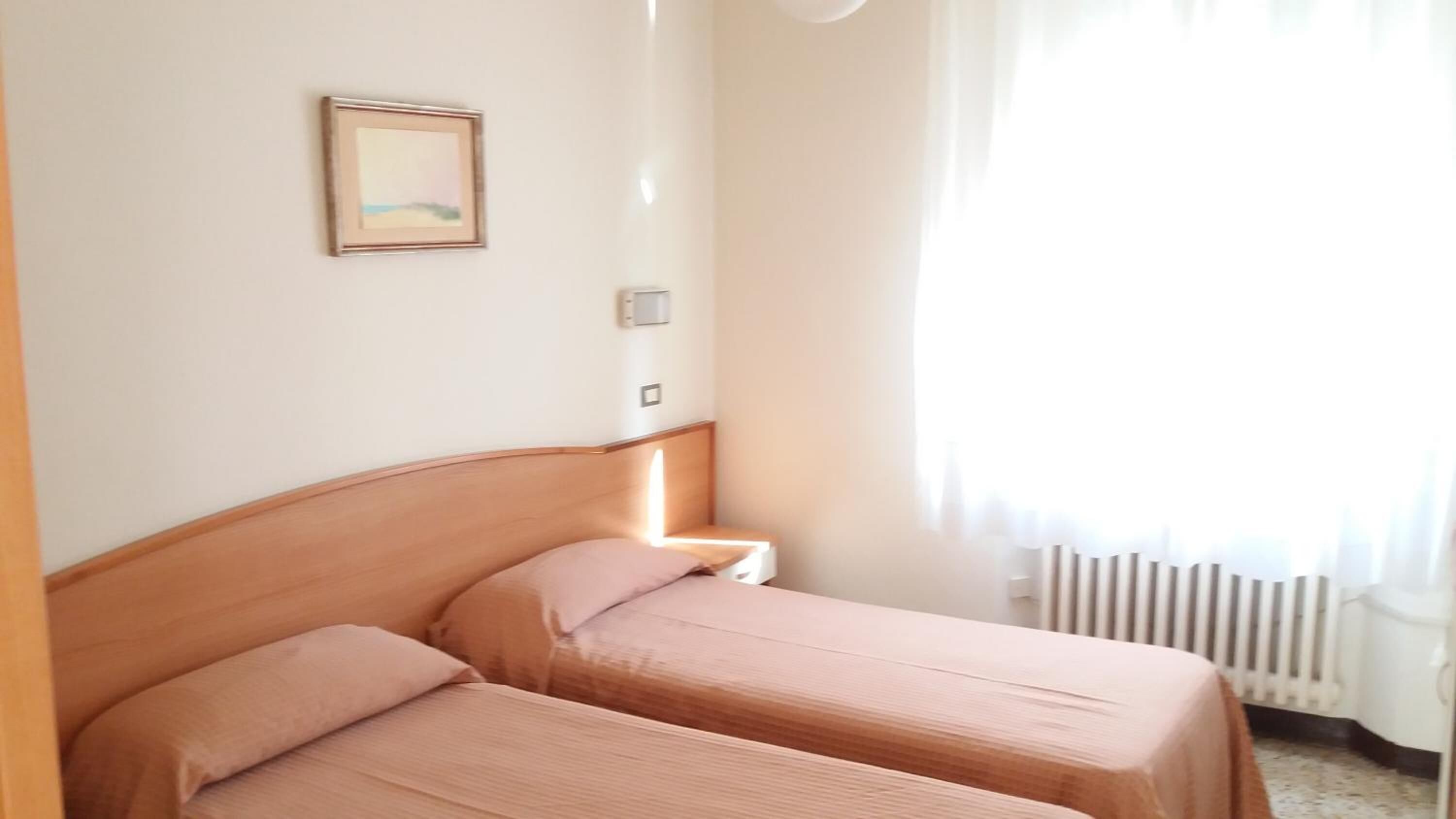 Una habitación con dos camas, una mesita de noche, un cuadro en la pared y una ventana con cortinas.