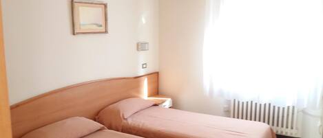 Una habitación con dos camas, una mesita de noche, un cuadro en la pared y una ventana con cortinas.