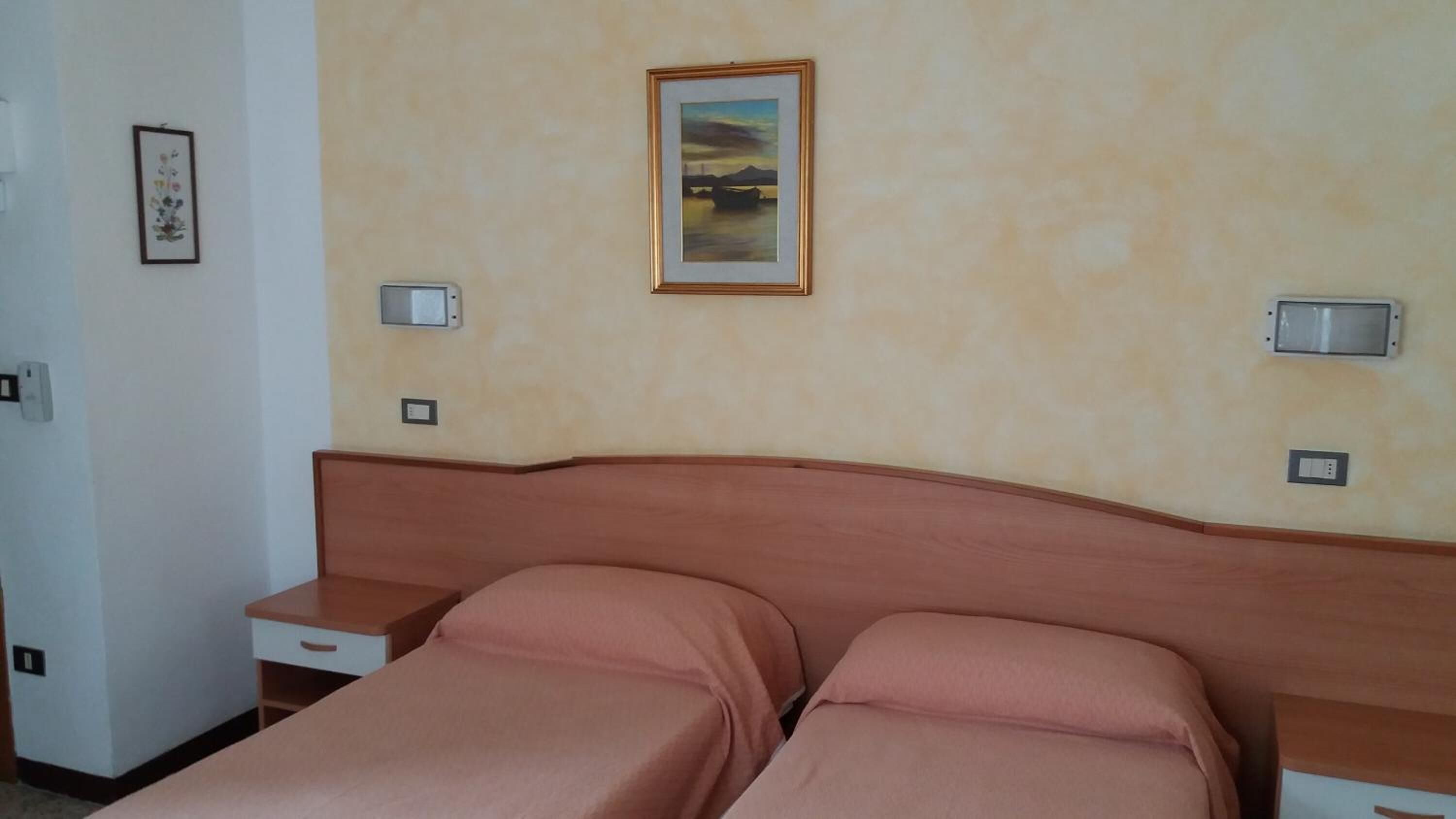 A hotel room with a bed, bedside tables, a painting, and wall-mounted lights.