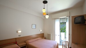 A hotel room with two beds, a desk with a chair, a television, and a window with a view of greenery. - Moretti (Senigallia)