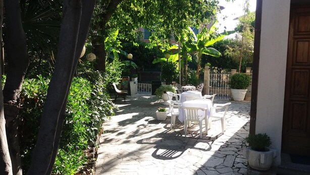 An outdoor patio with stone flooring, white plastic furniture, and potted plants.